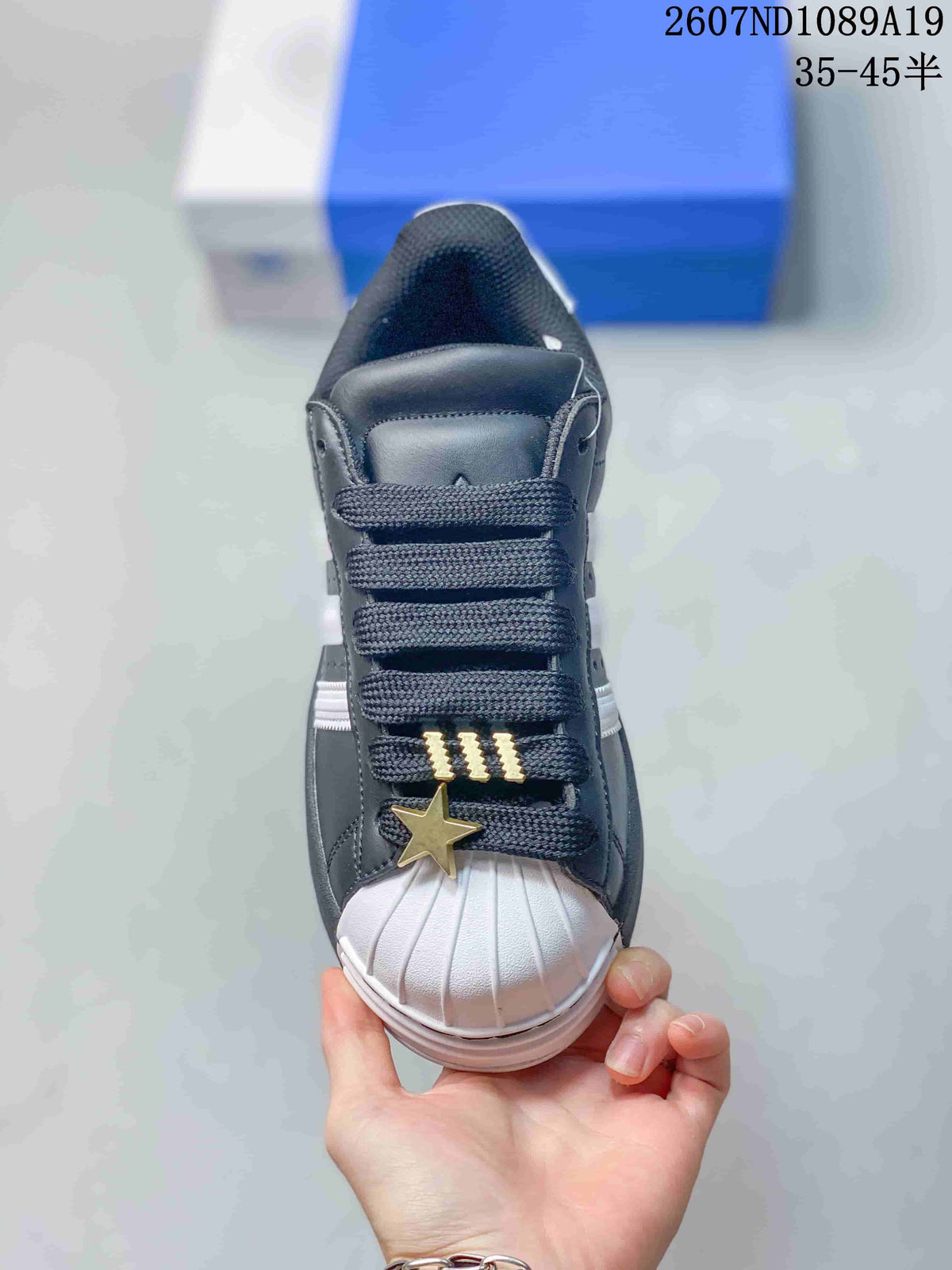 Top view of one sneaker showing black laces, gold-tone star ornament and white ribbed shell toe.