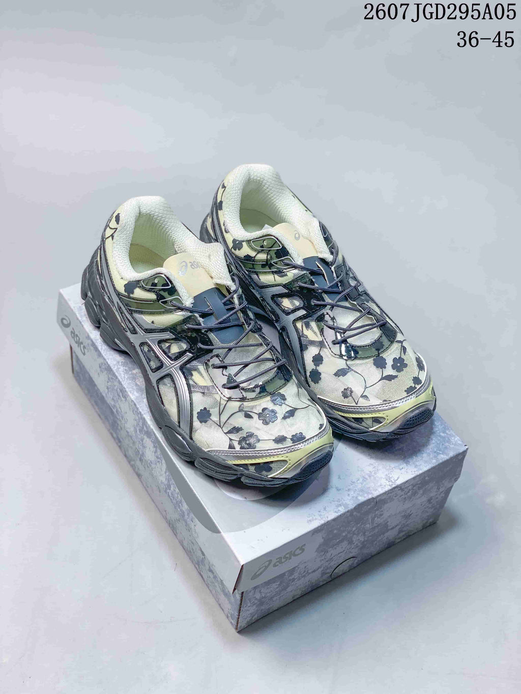 Pair of light green and cream ASICS Gel-Cumulus 16 sneakers with dark floral detailing on a shoe box.