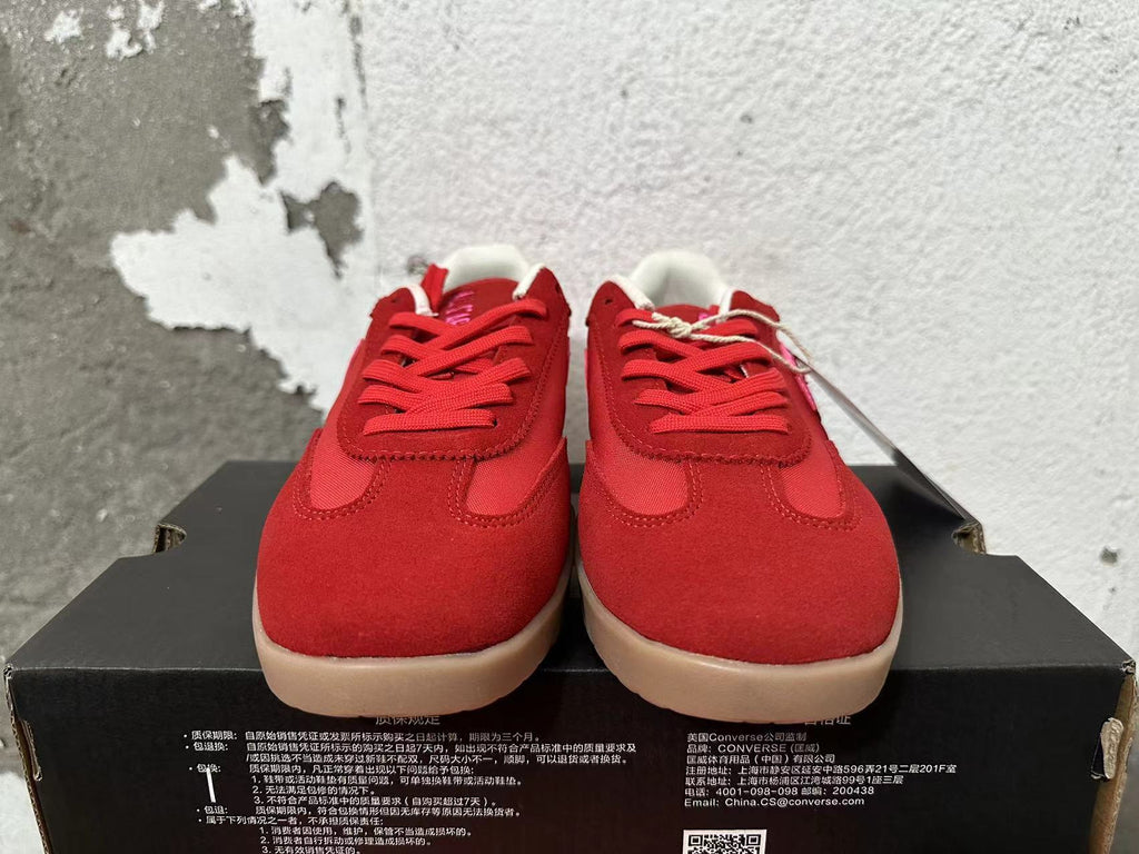 Front view of red lace-up Converse sneakers with pink accents and tan-colored soles.