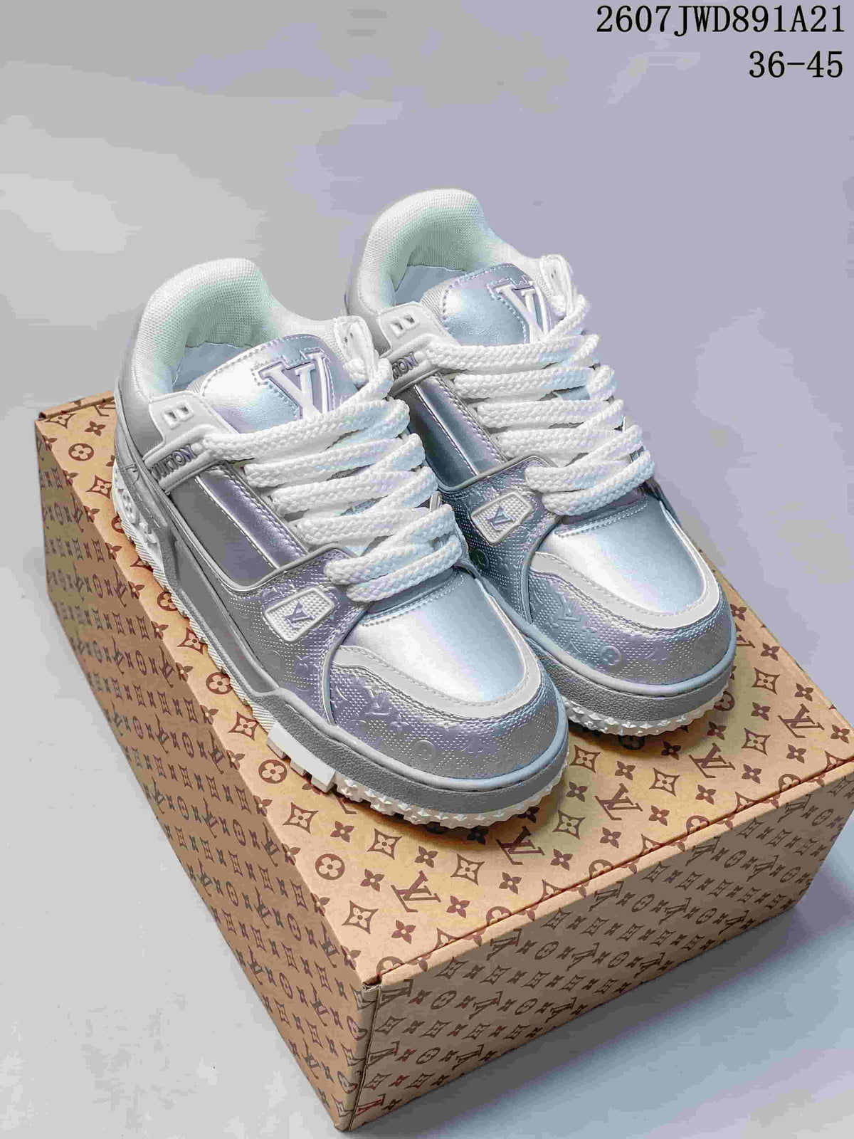 Pair of silver and white Louis Vuitton Trainer Maxi sneakers displayed on a patterned shoe box.