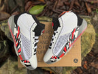 Overhead angled view of both shoes showing the white uppers, black tongues, and red and black side accents.