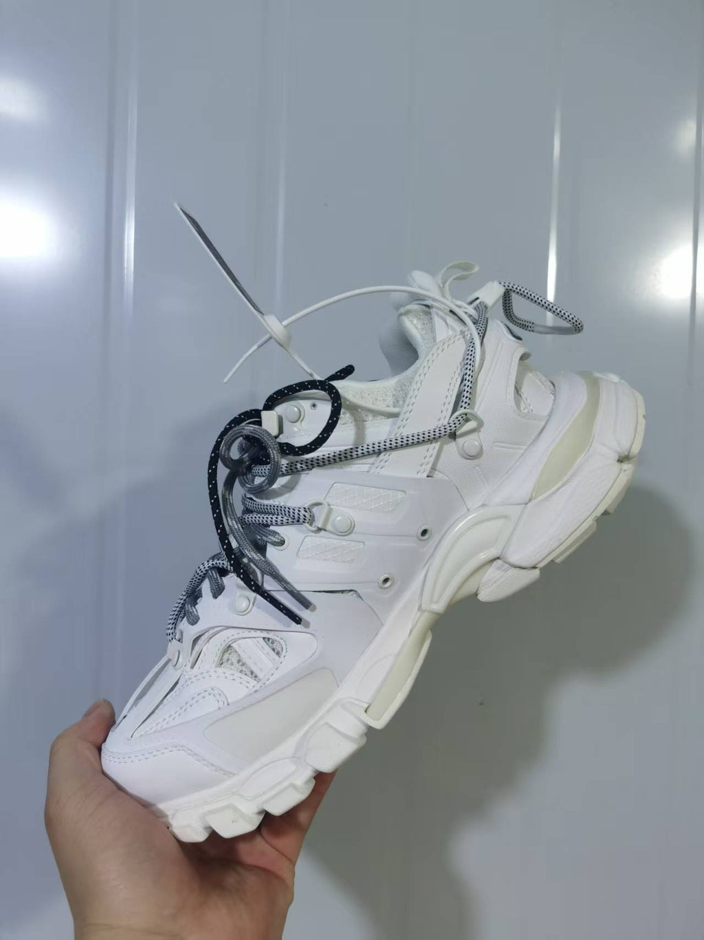Side and rear view of the white sneaker showing its layered panels, lace system, and sculpted sole.