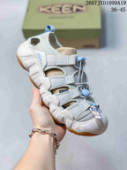 Angled side view showing the white and gray upper, blue accents, closed toe, heel opening, and tan outsole.