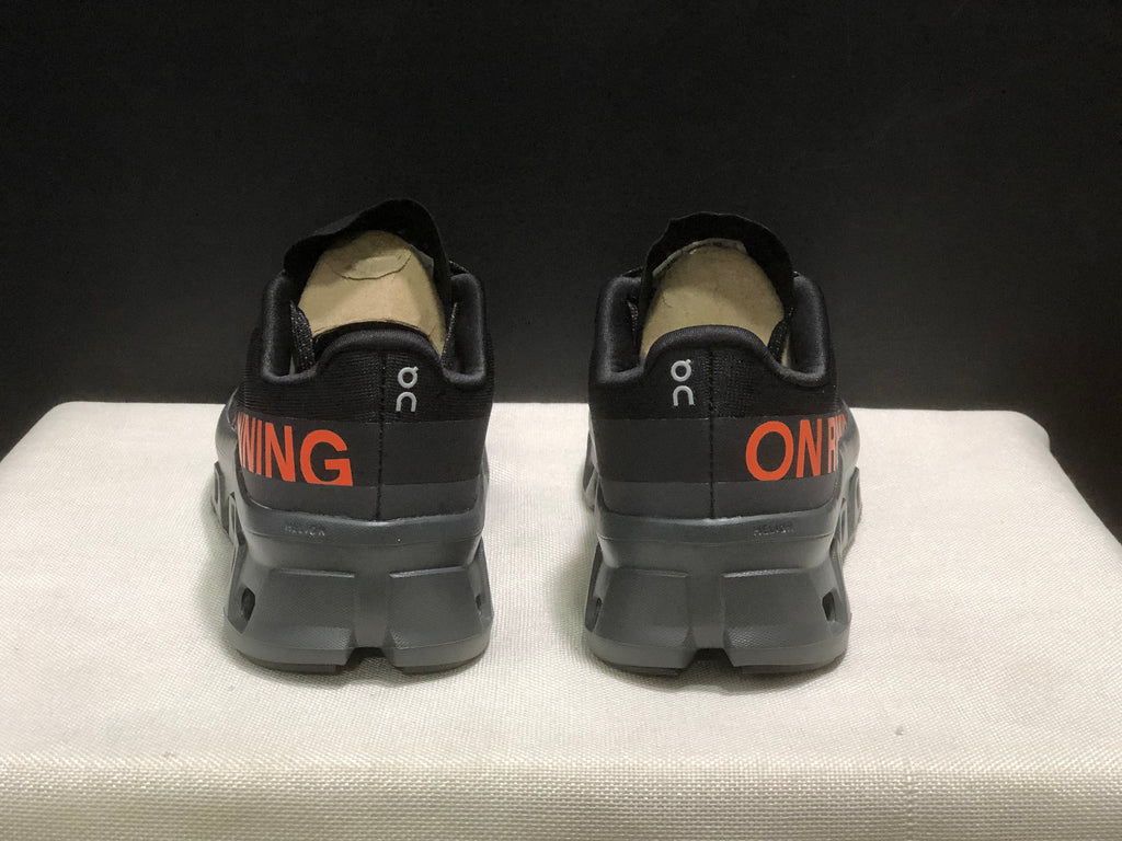 Rear view of the black sneakers showing padded collars, heel branding, and orange side graphics.