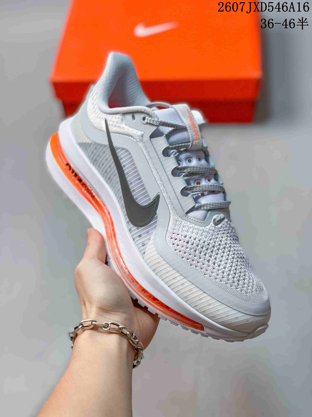Angled side view of the sneaker showing the perforated upper, dark Nike Swoosh, gray panels, and orange midsole element.