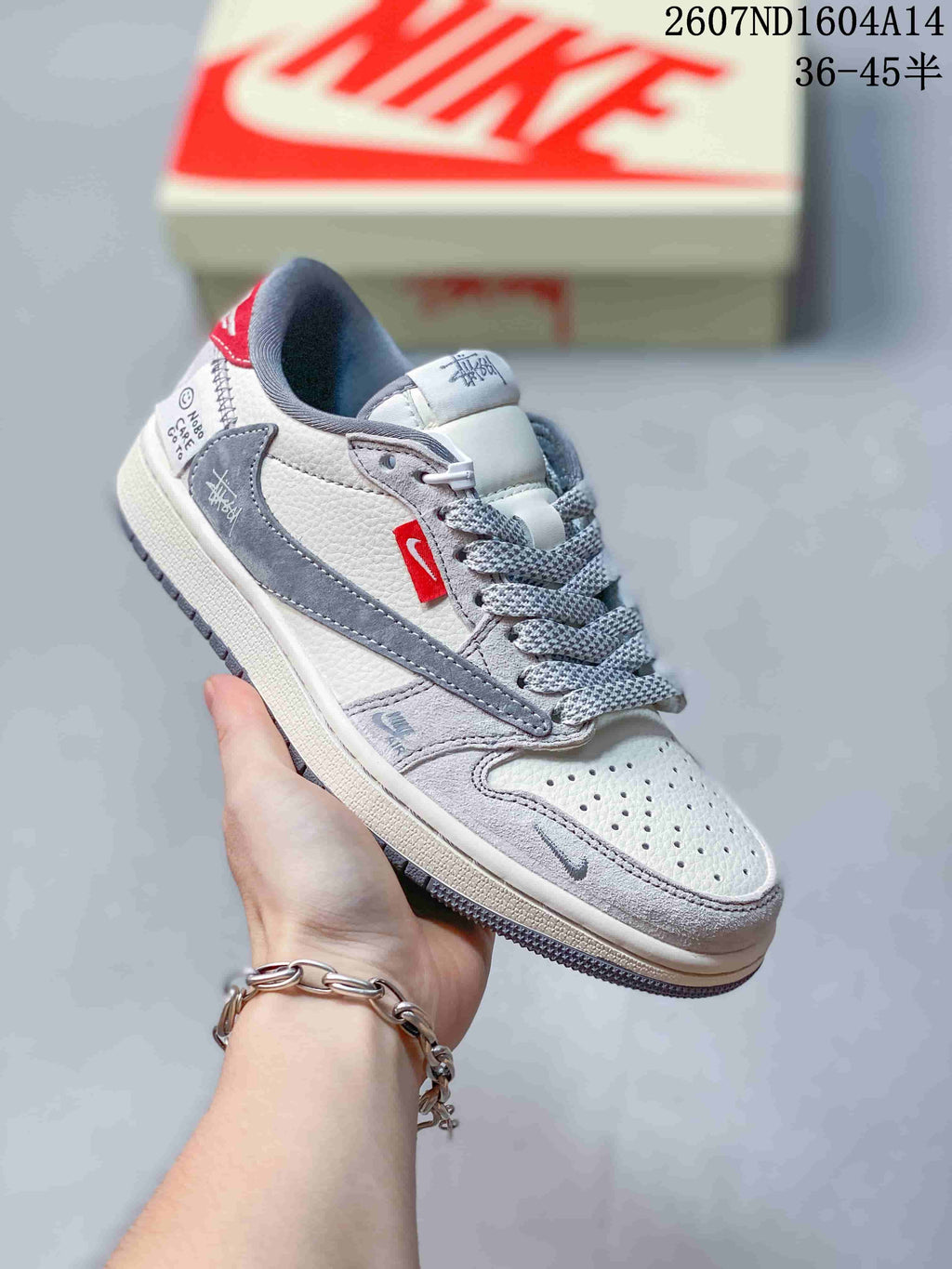 Angled side view of the sneaker showing the perforated toe, gray overlays, red side accent, and branded details.