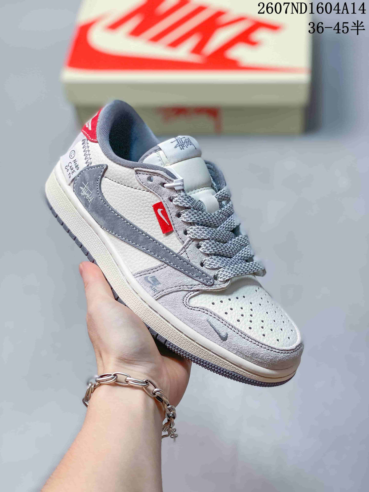 Angled side view of the sneaker showing the perforated toe, gray overlays, red side accent, and branded details.