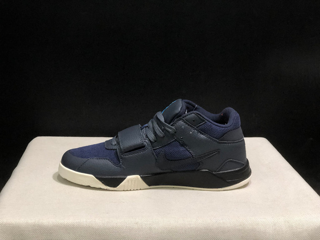 Lateral side profile showing the dark upper, layered panels, side branding, strap, and cream outsole.