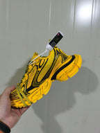 Close-up side view of a yellow and black lace-up sneaker showing the patterned upper, black detailing, and segmented outsole.