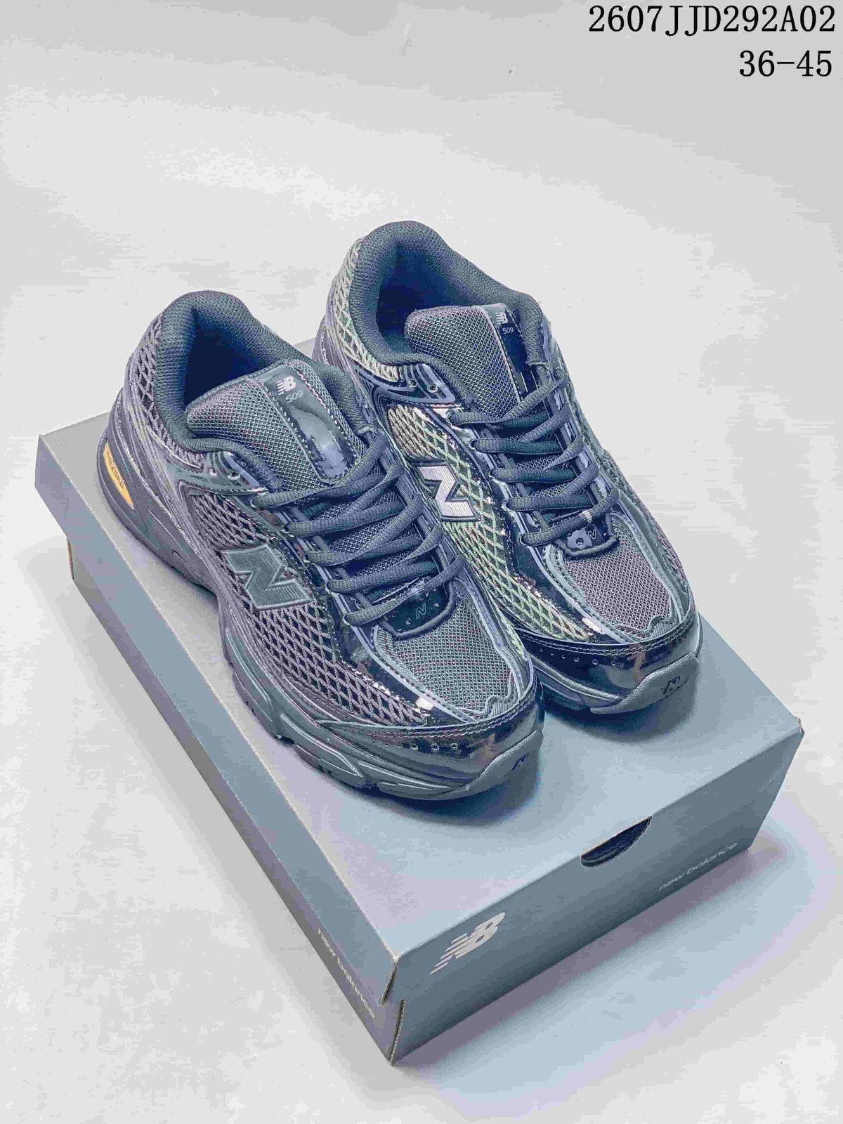 Pair of dark gray New Balance 509 sneakers shown from a front three-quarter angle on a New Balance shoebox; image text shows style code 2607JJD292A02 and EU size range 36–45.