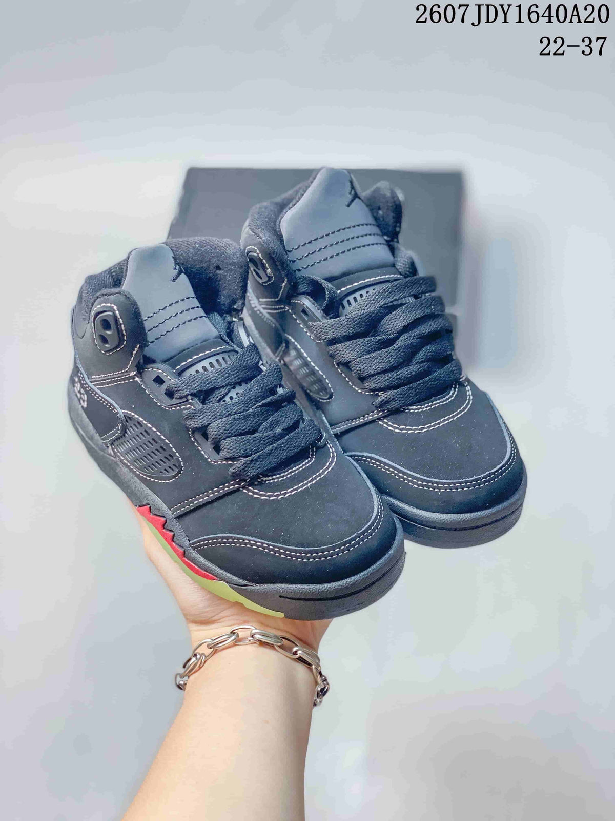 Pair of dark Jordan Air Jordan 5 Retro kids' sneakers shown from a front three-quarter angle, with red accents and lime-green outsole details.