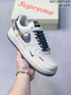Angled side view showing the white upper, navy Swoosh and heel accents, patterned laces and grey outsole.
