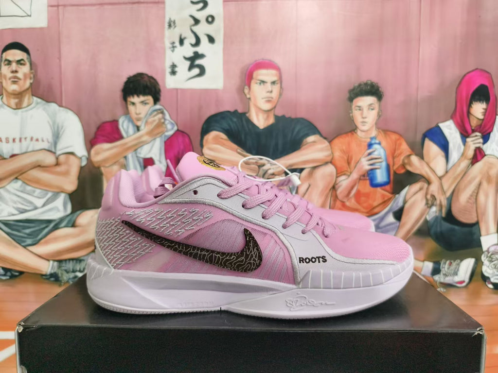 Side view of pink and light gray shoes with a dark patterned Swoosh and ROOTS lettering