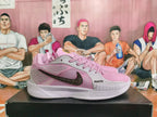 Side view of pink and light gray shoes with a dark patterned Swoosh and ROOTS lettering