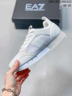 Side profile of a white Emporio Armani EA7 sneaker with textured mesh panels, tonal overlays, lace-up closure, and serrated outsole.