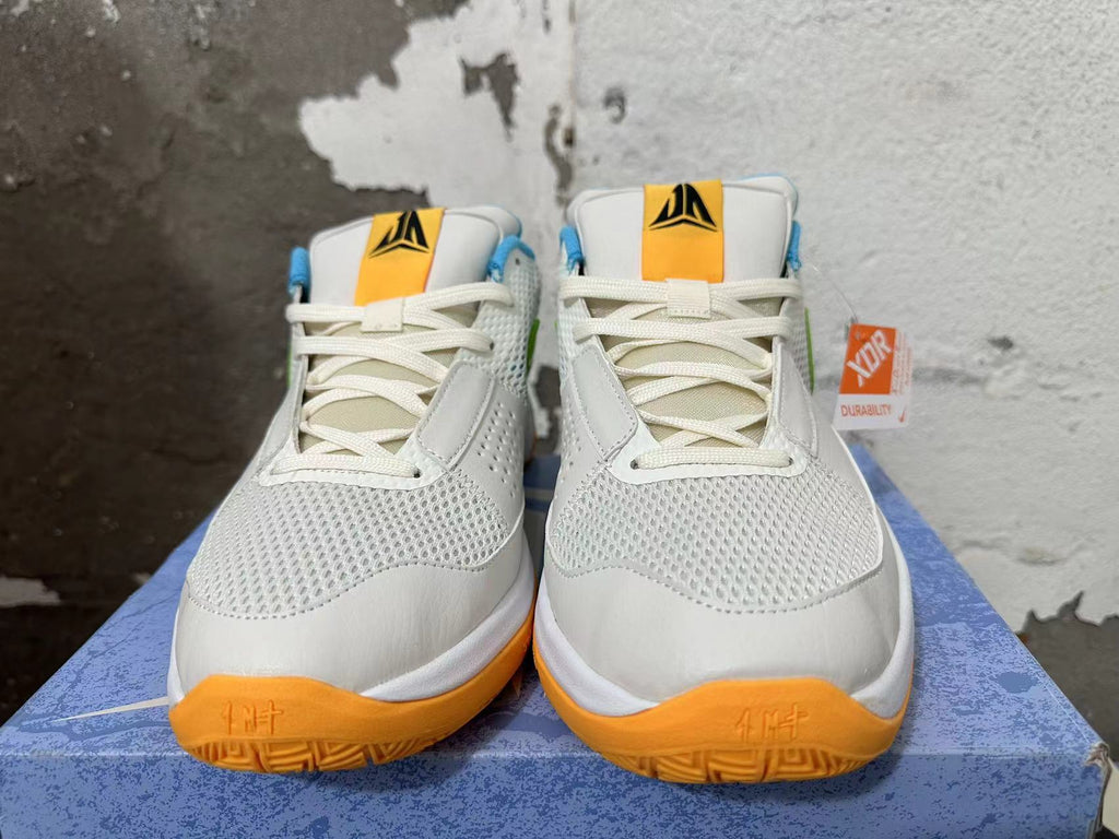Front view of white Nike Ja 1 shoes with mesh toe panels, cream laces, and orange outsole accents