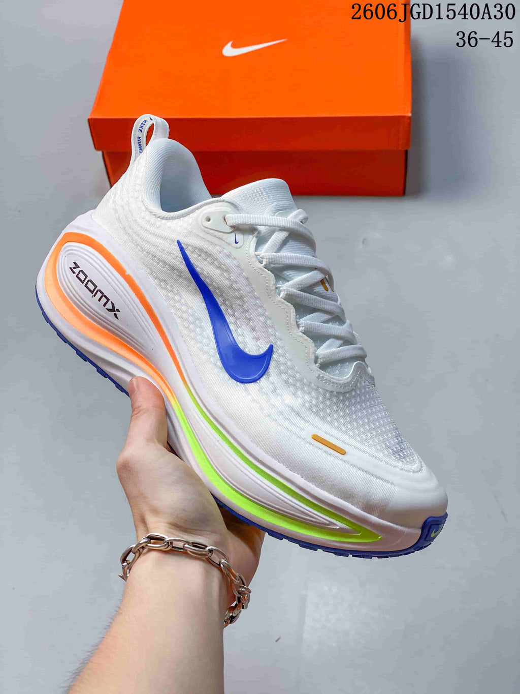 White Nike Vomero Plus running shoe with a blue Swoosh and colorful sole accents.