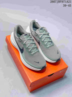 Pair of gray and muted green Nike Vomero 18 sneakers displayed on an orange Nike shoebox.