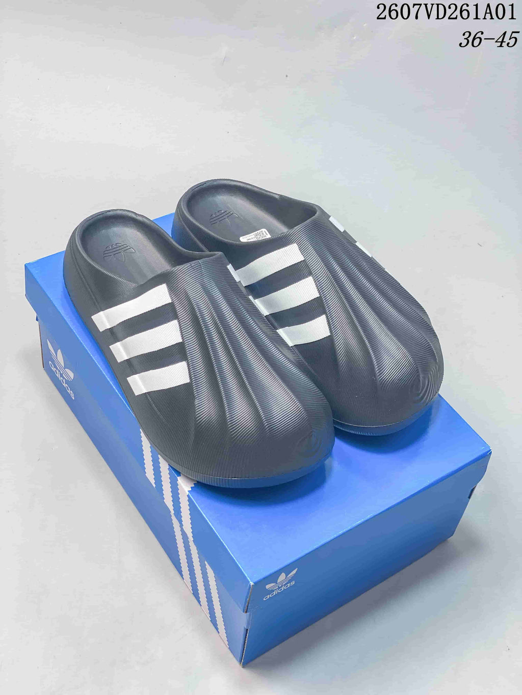 Pair of dark adidas adiFOM Superstar Mule clogs with white stripes, shown on a blue shoe box.