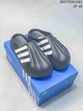 Pair of dark adidas adiFOM Superstar Mule clogs with white stripes, shown on a blue shoe box.
