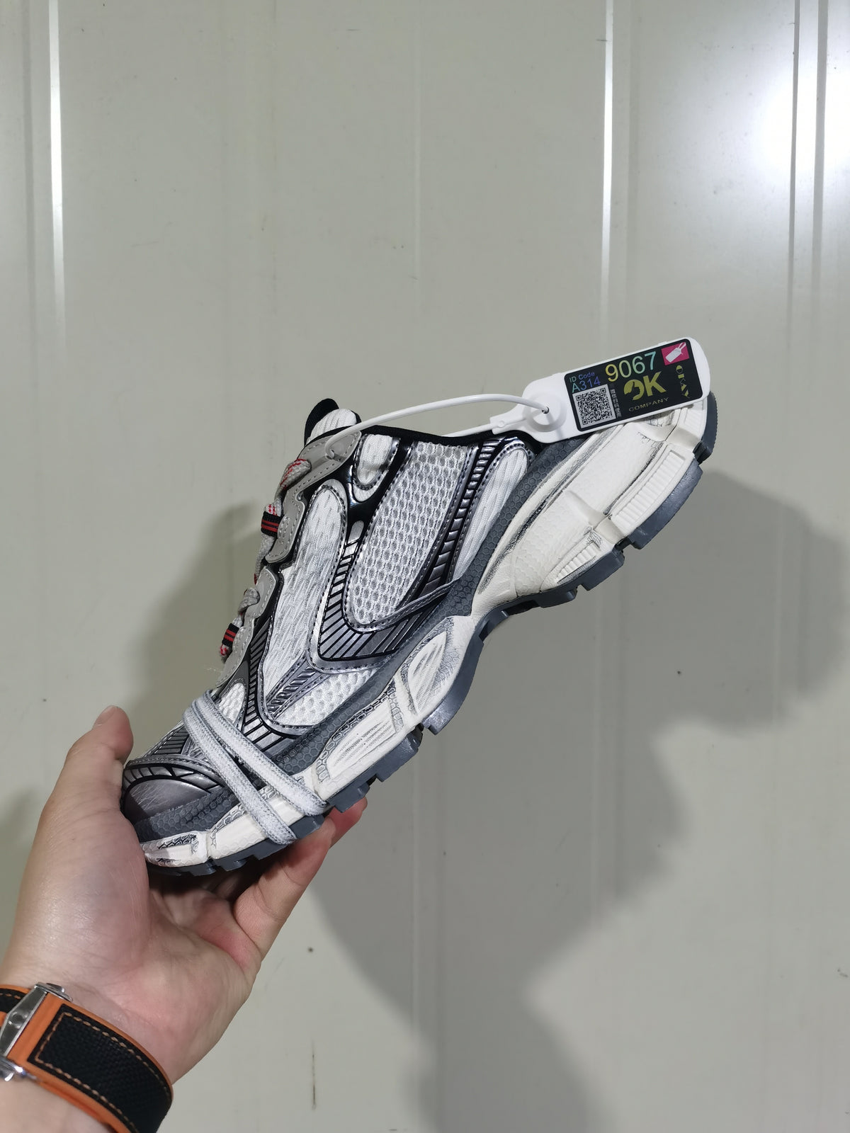 Angled outsole and side view of the grey and white sneaker with black trim, red accents and a hanging product tag.