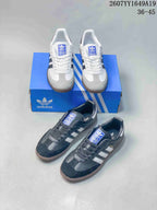 White and black Adidas Samba sneakers shown together with a blue Adidas shoebox.