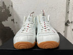 Front view of white Nike Foamposite sneakers with white laces, tongue badges, and gum-colored toe outsoles