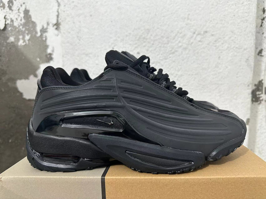 Side view of a black Nike Air Max SNDR sneaker showing ridged panels and a heel cushioning window.