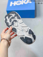 Close view of the sneaker outsole showing a white sole with dark patterned traction sections; a blue Hoka box is in the background.