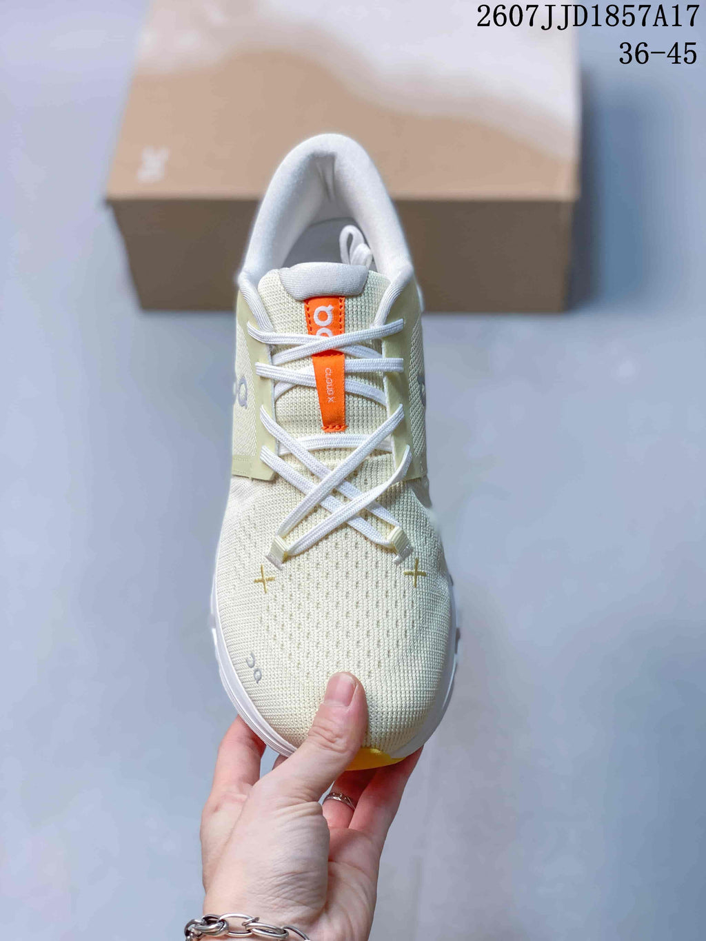 Top view of the sneaker showing white laces, orange tongue label, textured cream upper, and contrasting toe details.