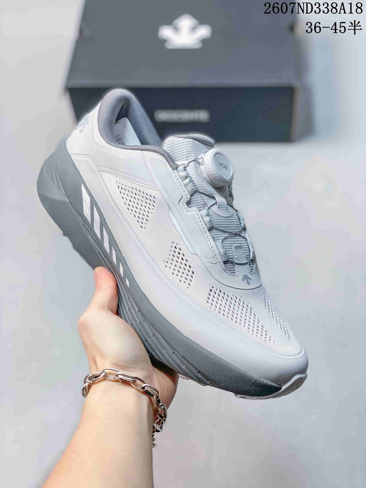 Side view of a white Descente D.F. Wire 3.0 sneaker held in hand, showing the perforated side panels, layered upper and textured outsole.
