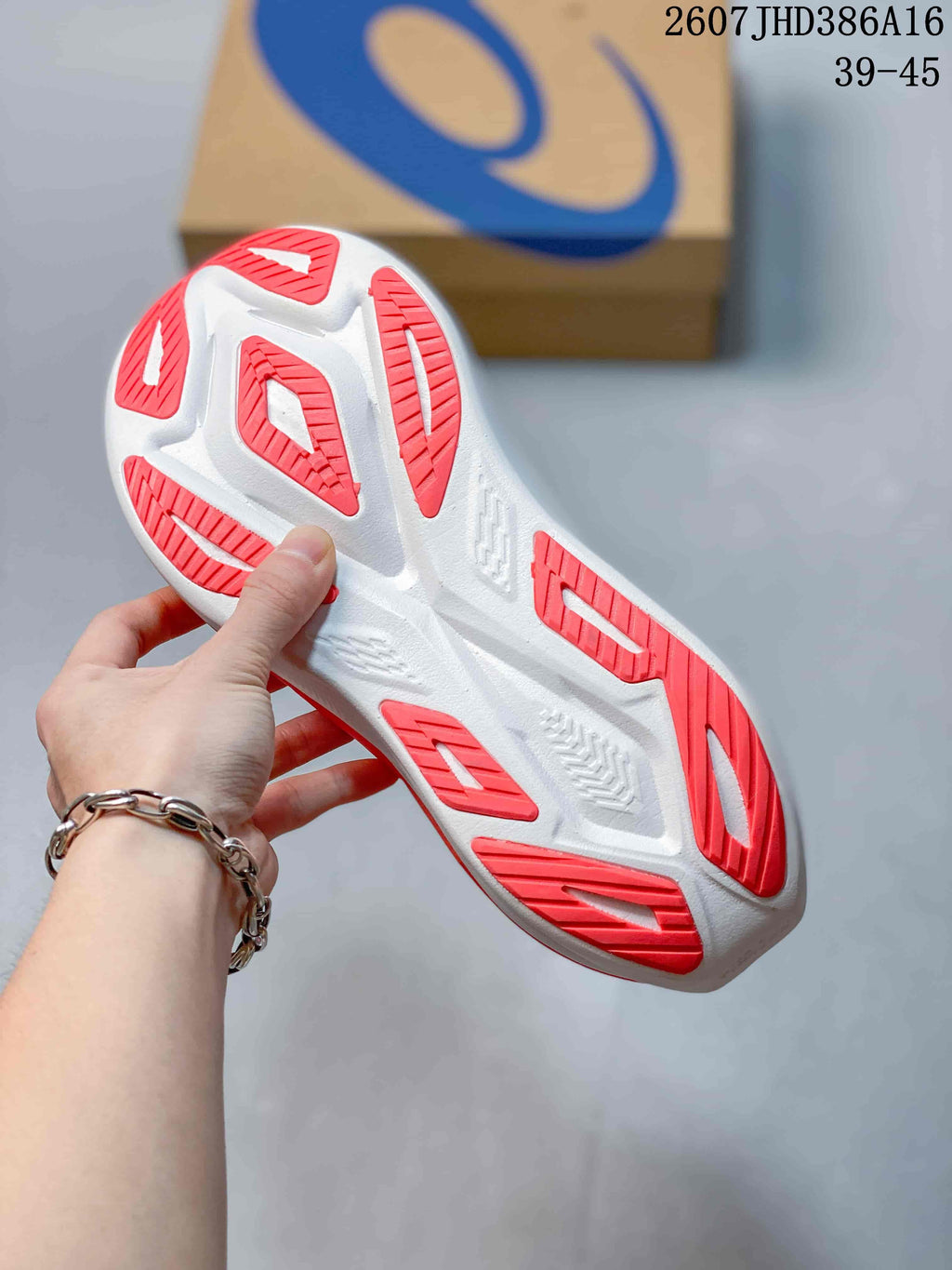 Close-up of the patterned outsole with red traction sections and an ASICS shoe box in the background.
