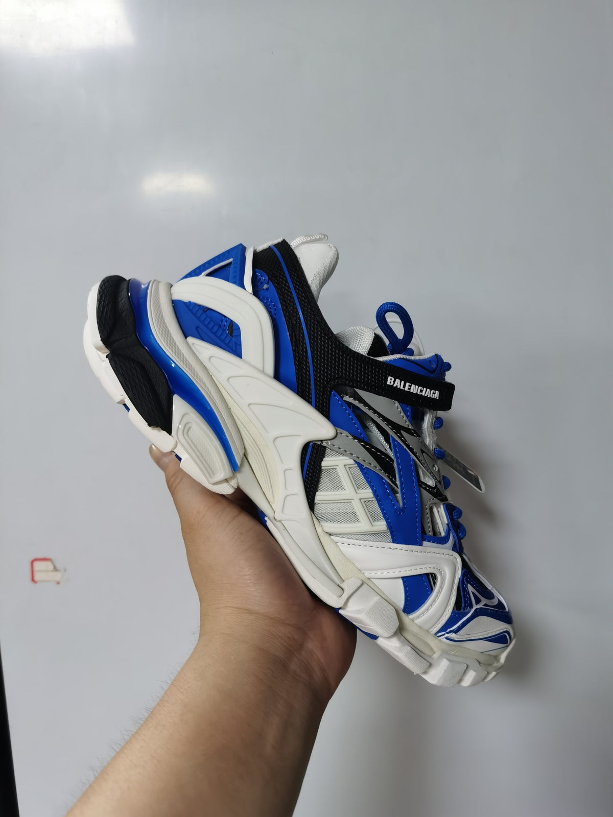 Angled rear and side view showing the layered panels, branded strap and segmented sole of the Balenciaga sneaker.