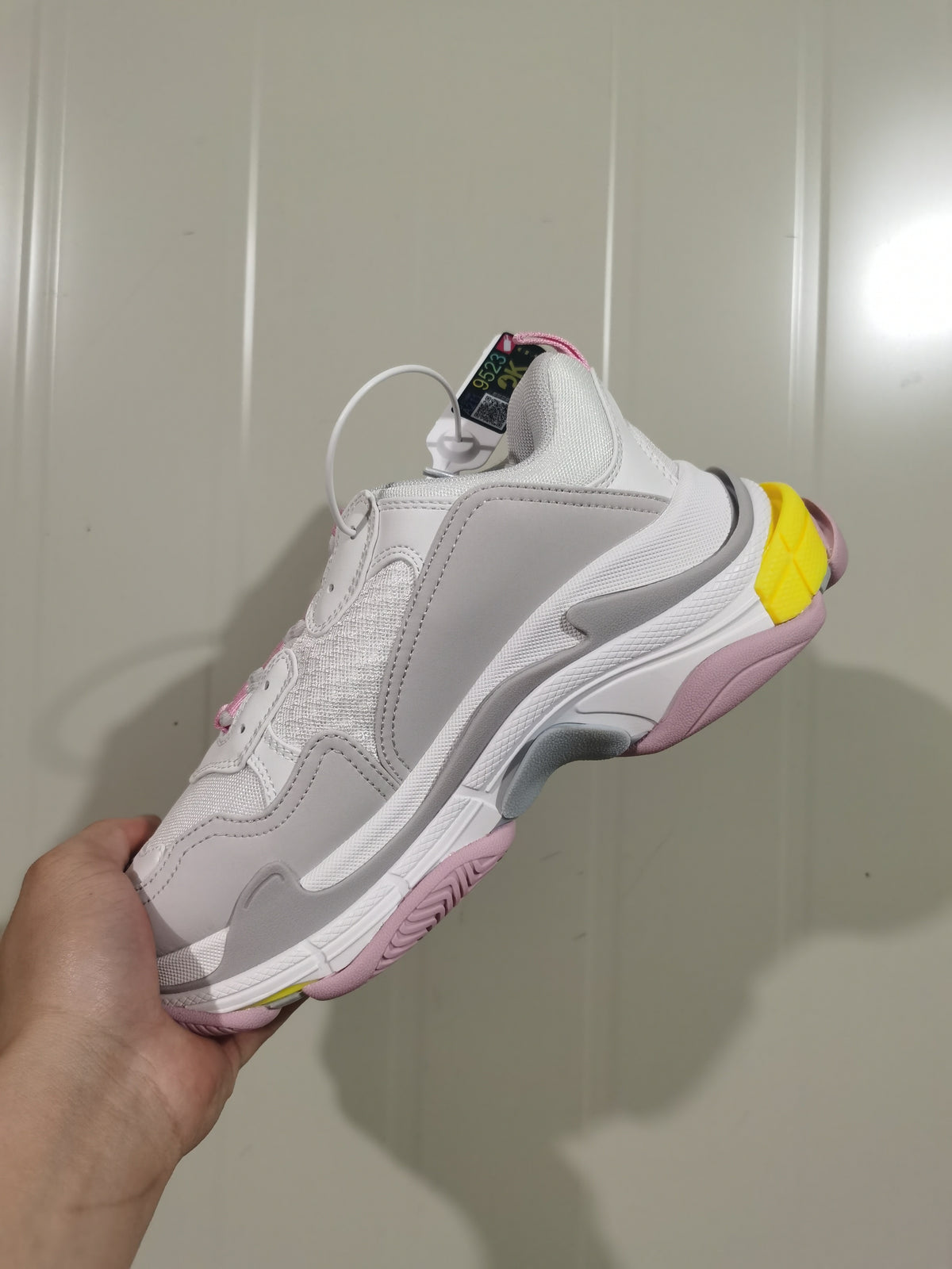 Side view of white Balenciaga Triple S sneakers with grey panels, pink outsole details and a yellow heel accent.