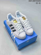 Pair of white and black Adidas Superstar sneakers displayed on a blue Adidas shoe box.