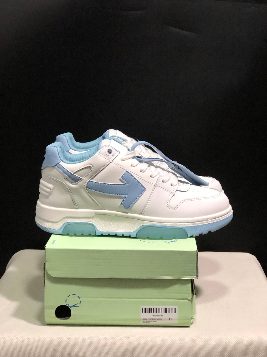Side view of the white and light blue low-top sneakers showing layered panels, arrow-style side detailing and padded collars.