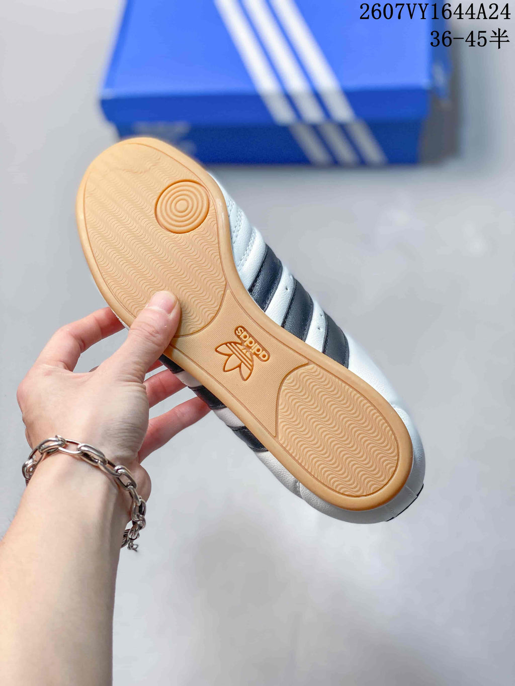 Underside view of a white adidas sneaker showing the gum-colored textured outsole and circular forefoot traction detail.