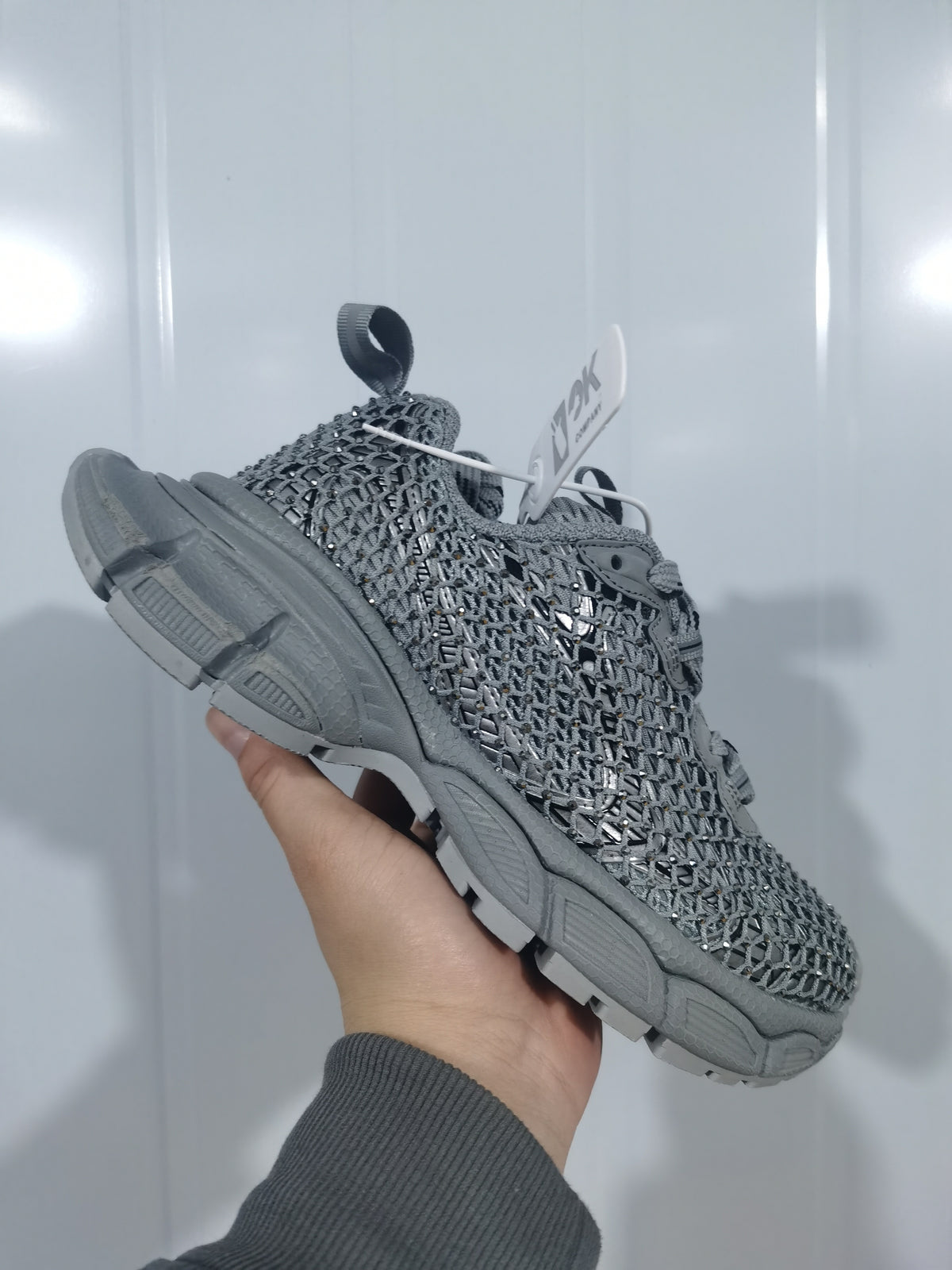 Side view of the grey and crystal sneaker showing its textured upper, matching laces, padded collar, and molded outsole.
