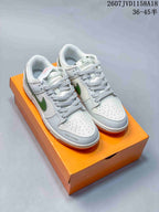 Pair of white low-top sneakers with green Swoosh details and patterned laces displayed on an orange shoe box.