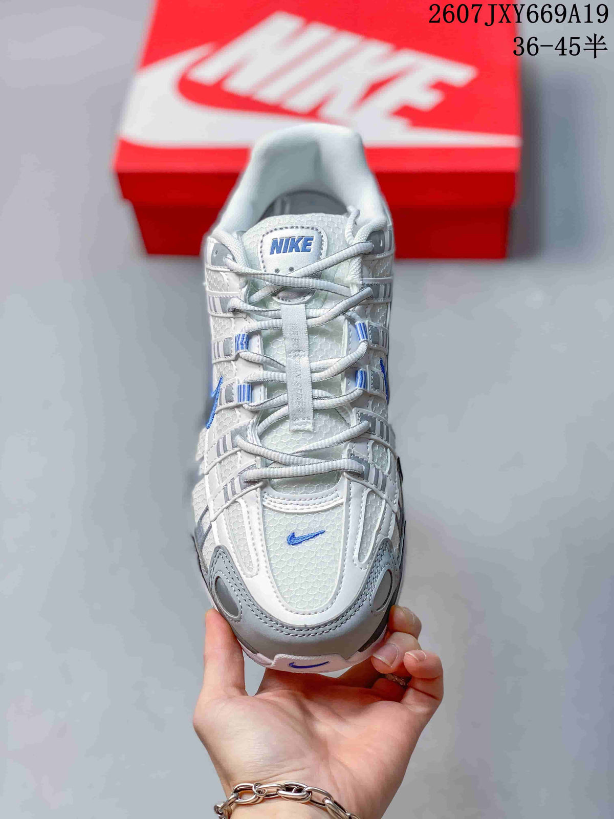 Top-down view of the sneaker showing the white mesh-like upper, grey overlays, blue details, and laces.