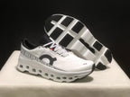 Angled view of the white sneakers with one shoe lifted to show the segmented black-and-white outsole.
