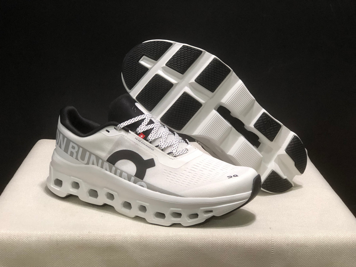 Angled view of the white sneakers with one shoe lifted to show the segmented black-and-white outsole.
