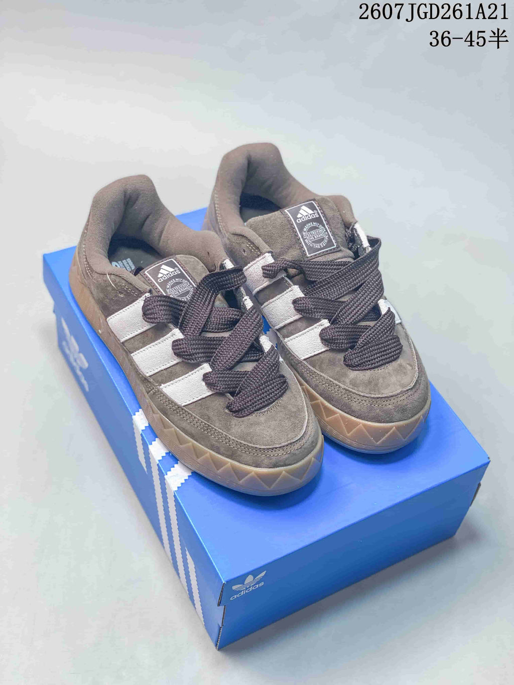 Pair of brown and white Adidas low-top sneakers displayed on a blue Adidas shoebox, with dark laces and gum-colored soles.