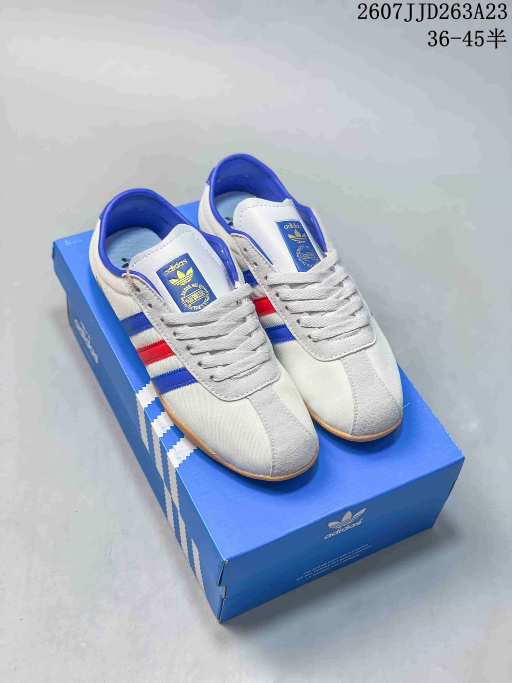 Pair of white adidas Tokyo sneakers with blue and red stripes displayed on a blue adidas shoe box.