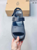 Top view of a black open-toe sandal showing the adjustable strap, textured footbed, heel strap, and UGG branding, with product code 2607JDD245A15 and size range 36–40 visible.