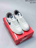 Pair of white and navy Nike low-top sneakers displayed on a red shoebox, with a gum-colored outsole visible.