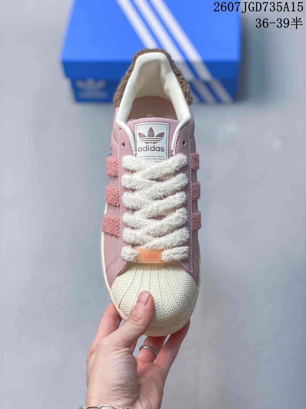 Top view of a pink sneaker with a shell toe, white textured laces, adidas tongue branding and textured side stripes.