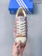 Top view of a pink sneaker with a shell toe, white textured laces, adidas tongue branding and textured side stripes.