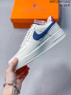 Side profile of the white low-top sneaker with a navy-blue Swoosh-style accent, layered panels, and raised midsole.