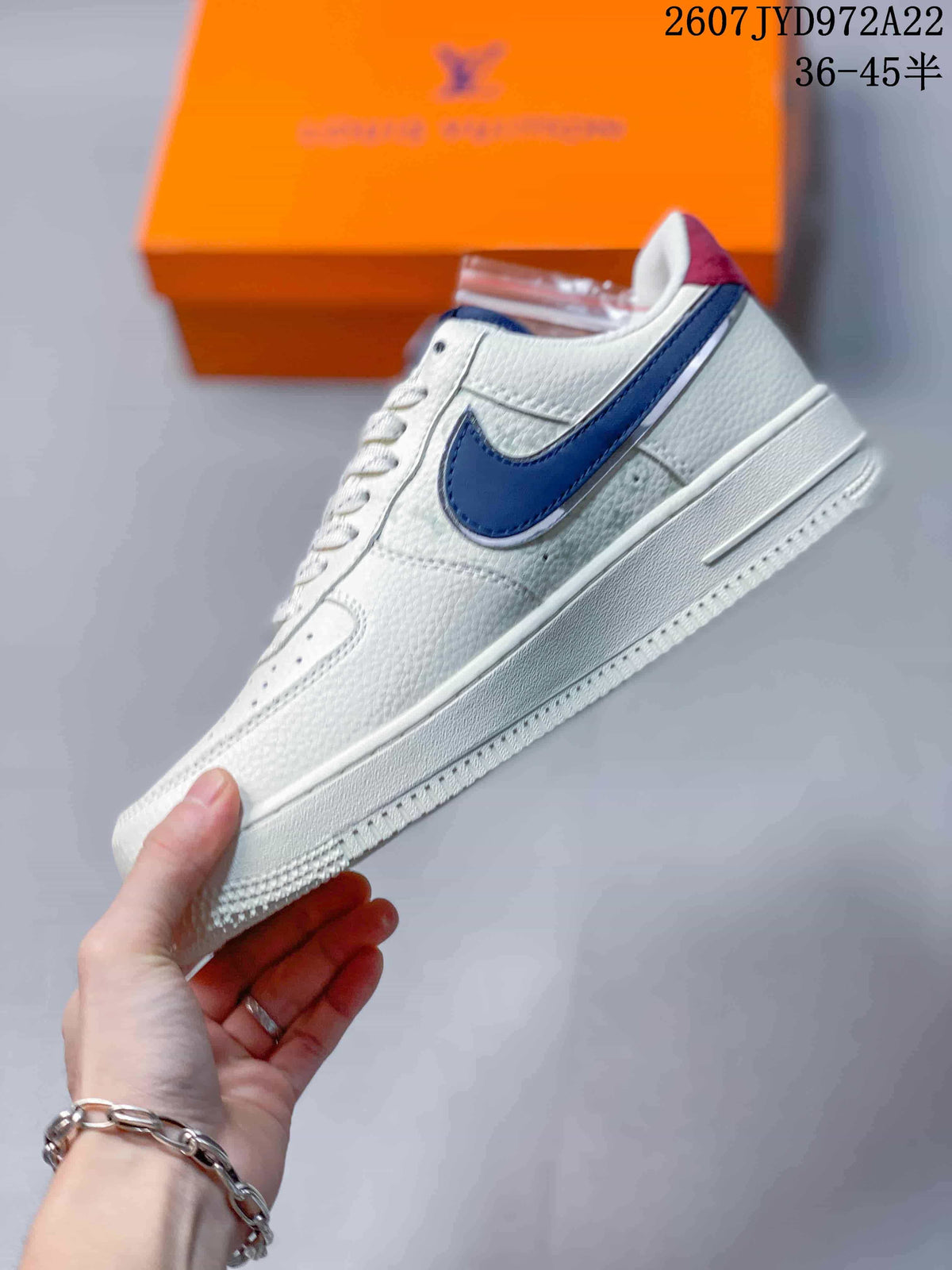 Side profile of the white low-top sneaker with a navy-blue Swoosh-style accent, layered panels, and raised midsole.